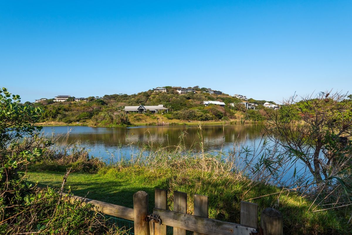 A scenic view overlooking a tranquil lake with surrounding natural landscape and distant residential properties on the hillside.