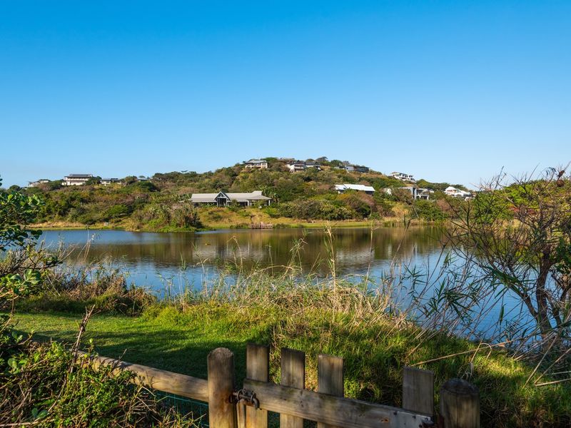 A scenic view overlooking a tranquil lake with surrounding natural landscape and distant residential properties on the hillside.