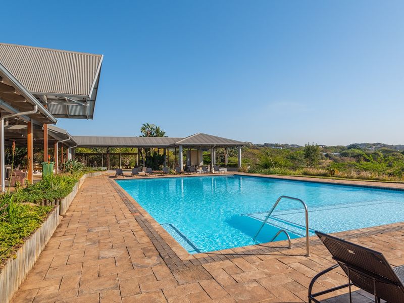 A well-maintained outdoor swimming pool area featuring a paved deck, covered patio structure, and scenic landscape views.