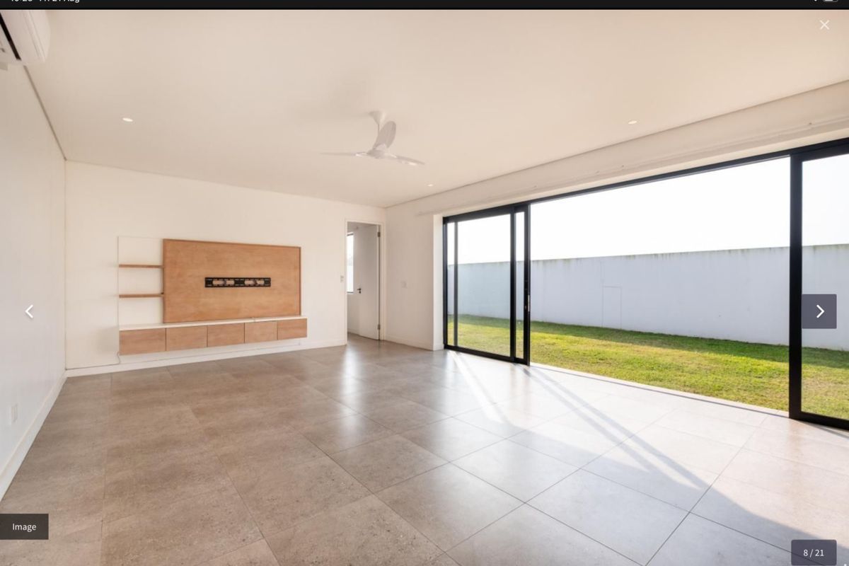 Spacious, modern living area featuring large format floor tiles, a built-in media console, and expansive sliding glass doors opening to a private garden.