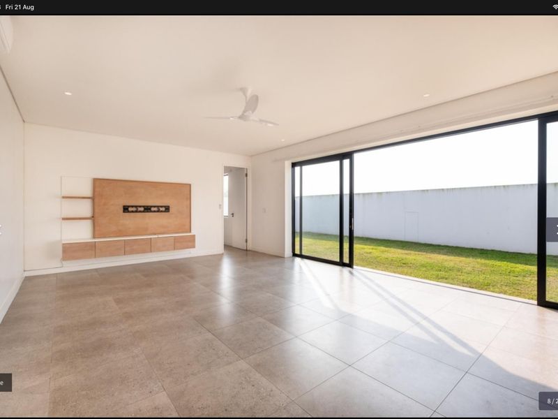 Spacious, modern living area featuring large format floor tiles, a built-in media console, and expansive sliding glass doors opening to a private garden.