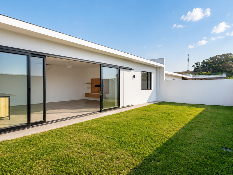 A modern townhouse rear exterior featuring a spacious lawn, high boundary walls, and large sliding glass doors opening into an open-plan living area.
