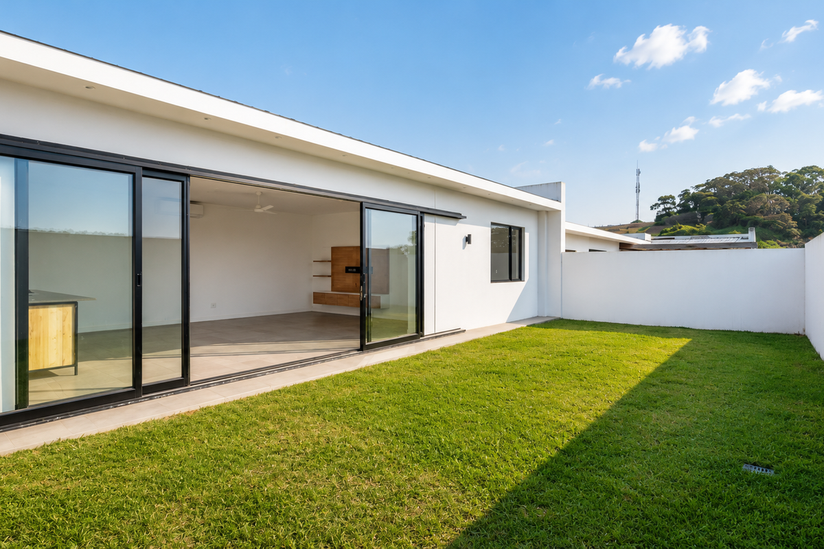 A modern townhouse rear exterior featuring a spacious lawn, high boundary walls, and large sliding glass doors opening into an open-plan living area.
