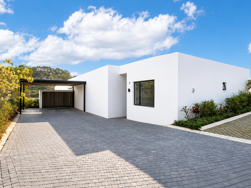 Modern townhouse exterior featuring a clean white facade, paved driveway, and integrated carport with timber detailing.