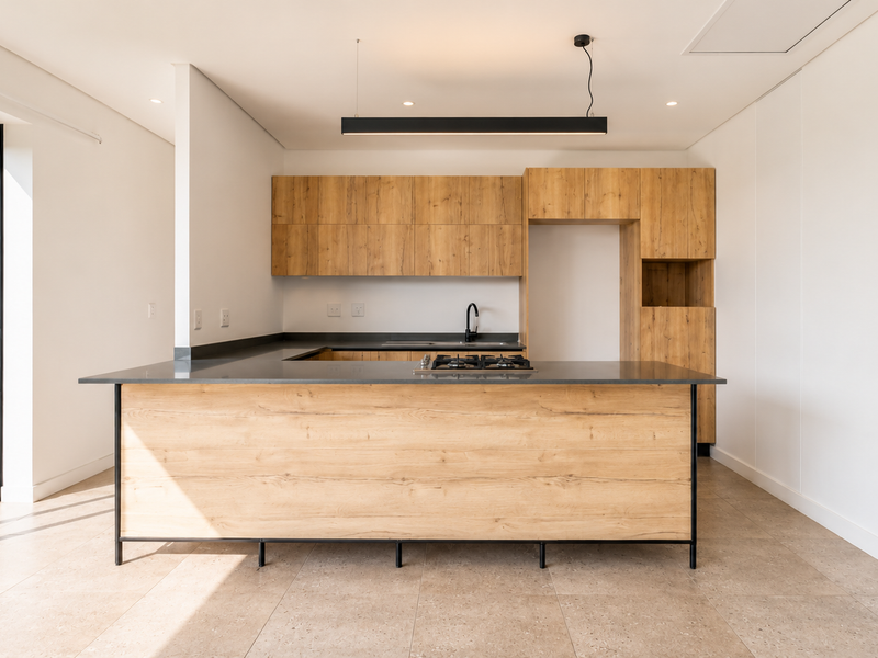 Modern kitchen featuring light wood-grain cabinetry, a central island with a gas hob, dark stone countertops, and direct access to the outdoor area.