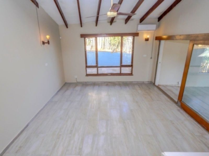 Spacious living area featuring exposed timber ceiling beams, tiled flooring, split-system air conditioning, and large windows providing natural light.