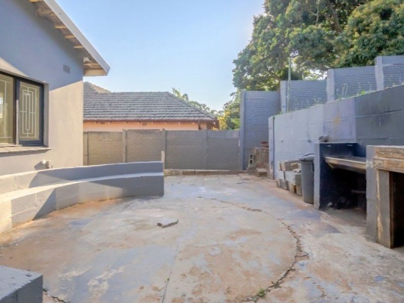 Outdoor patio area featuring a built-in braai, integrated concrete bench seating, and perimeter walling, offering a functional space for outdoor entertainment.