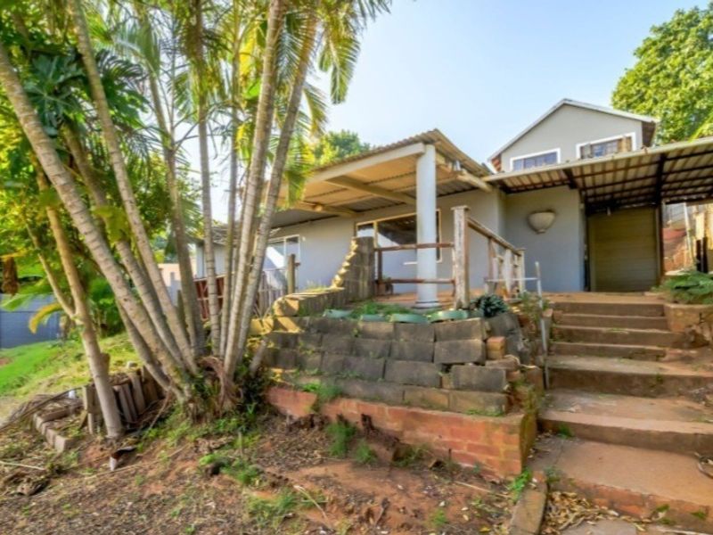 Rear view of the property featuring a covered patio area, concrete stairs, and a tiered retaining wall structure in a garden setting.