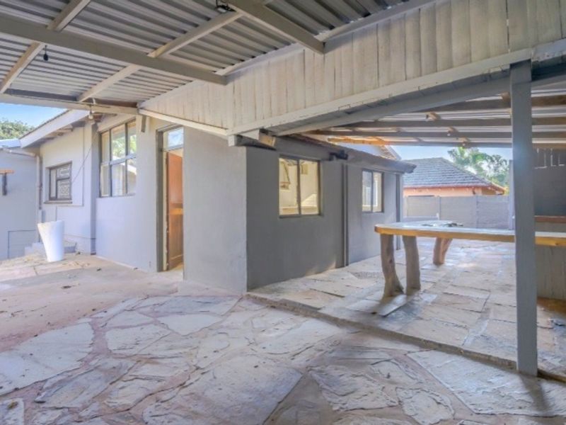 A covered outdoor patio area featuring stone paving, a built-in counter, and a corrugated metal roof structure.
