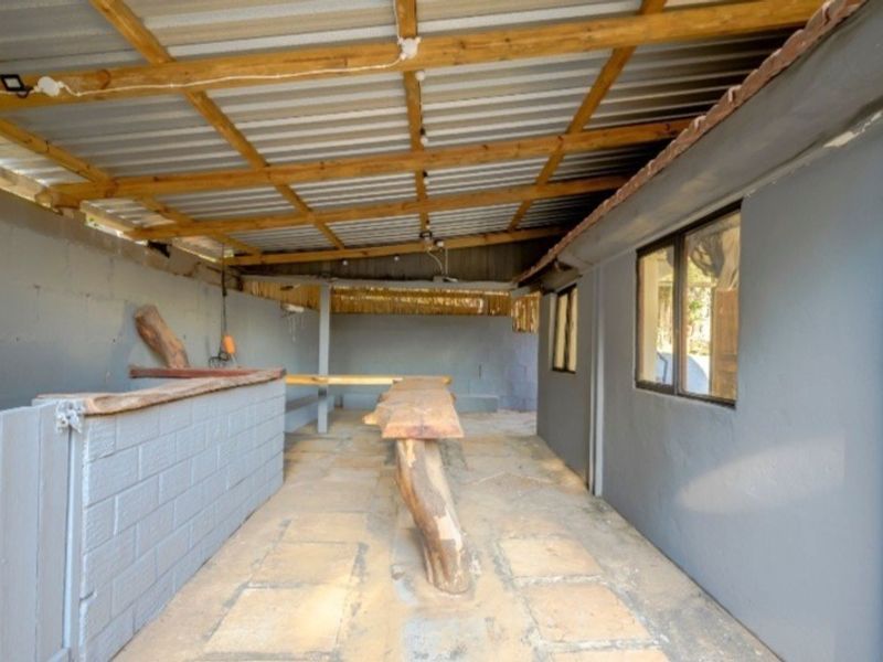 A covered outdoor patio area featuring a built-in brick bar counter, timber bench seating, and exposed roof rafters, offering potential for an entertainment space.