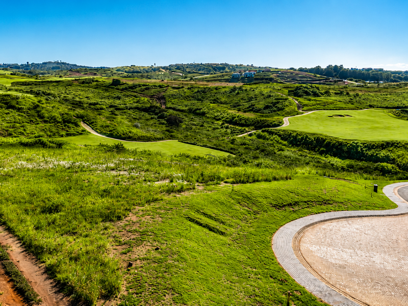 A scenic elevated view overlooking a lush green golf course landscape with a paved driveway in the foreground.
