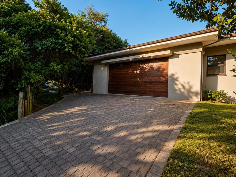 Front exterior view featuring a paved driveway, modern wooden garage door, and well-maintained landscaping.