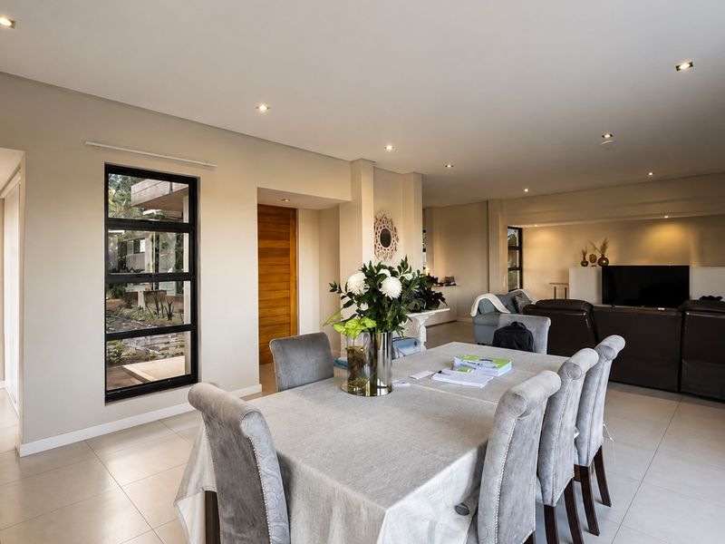 Spacious open-plan living and dining area featuring neutral tiled flooring, recessed lighting, and large black-framed windows providing natural light.