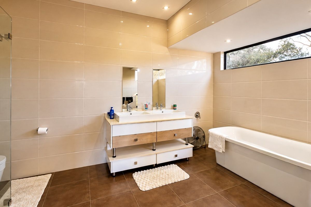 Modern bathroom featuring a double vanity, a sleek freestanding bathtub, a glass-enclosed shower, and neutral ceramic tiling throughout.