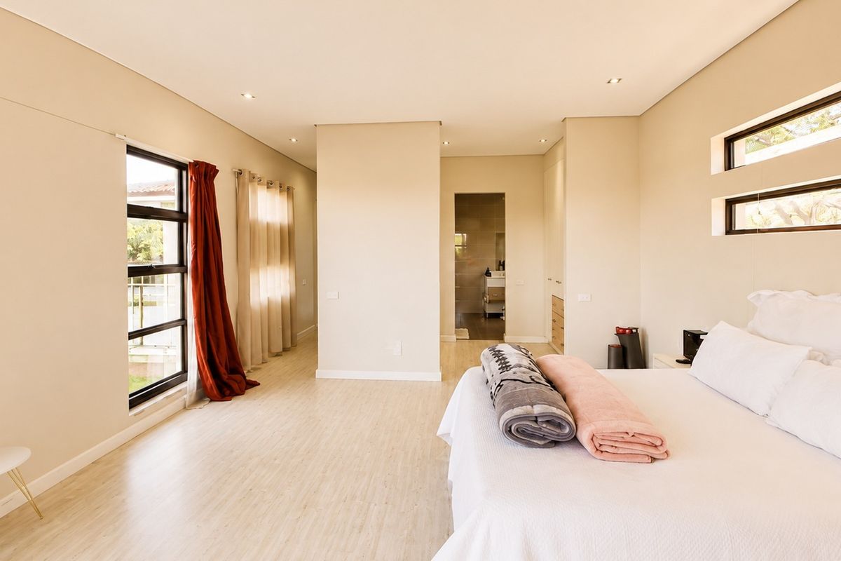 Spacious bedroom featuring light laminate flooring, recessed downlights, built-in cupboards, and an en-suite bathroom, offering a bright and modern living space.