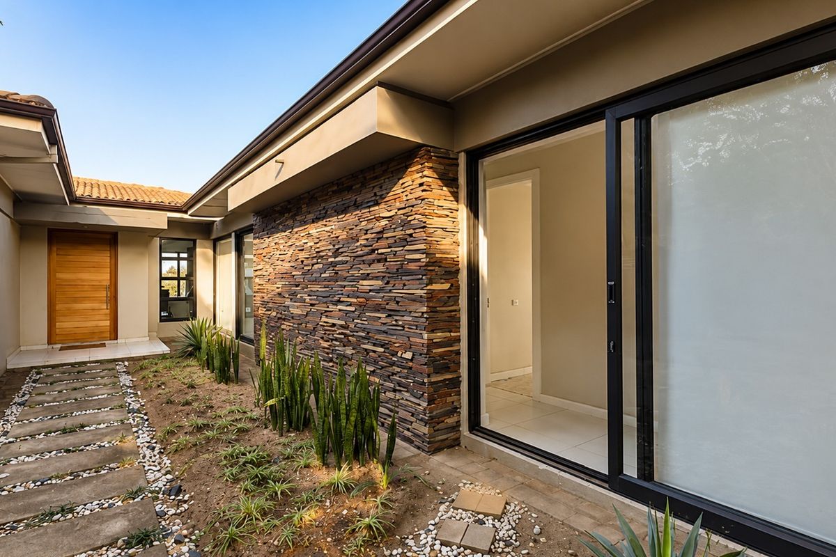 A modern rear exterior view featuring stone cladding, large sliding glass doors, and a paved walkway leading to a timber entrance door.