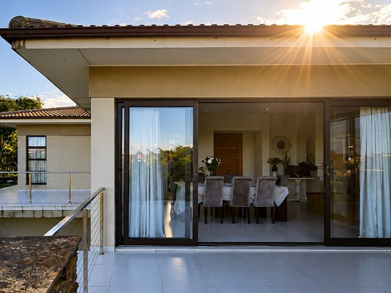 A spacious covered balcony featuring tiled flooring, stainless steel balustrades, and large sliding glass doors providing seamless access to the interior dining area.