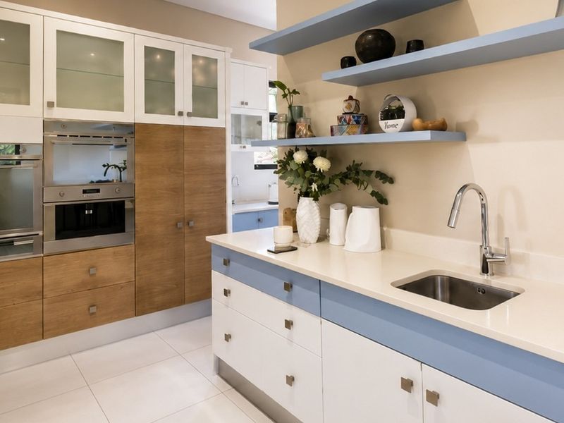 Modern kitchen featuring two-tone cabinetry, stone countertops, integrated appliances, floating shelves, and a sleek undermount sink with a contemporary mixer tap.