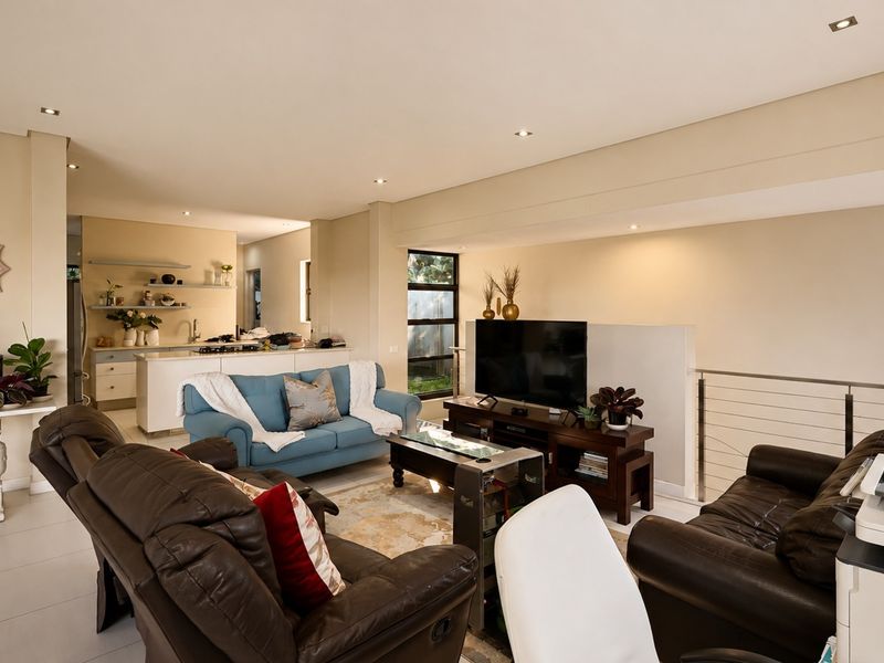 Spacious open-plan living area featuring a modern kitchen with island, tiled floors, recessed lighting, and a staircase with a contemporary metal balustrade.
