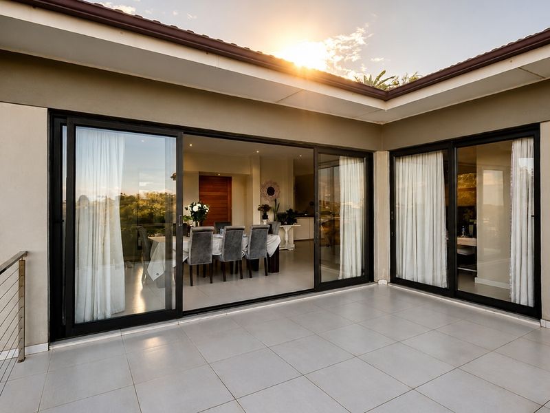 A spacious covered balcony featuring tiled flooring, stainless steel balustrades, and large sliding glass doors providing seamless access to the interior living area.