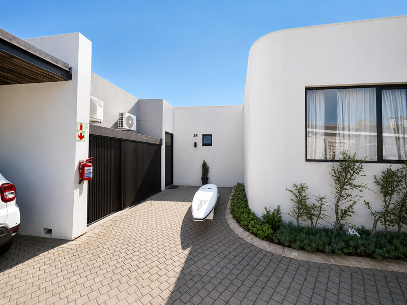 Modern townhouse front entrance featuring a paved driveway, carport, and clean white facade with landscaped garden beds.