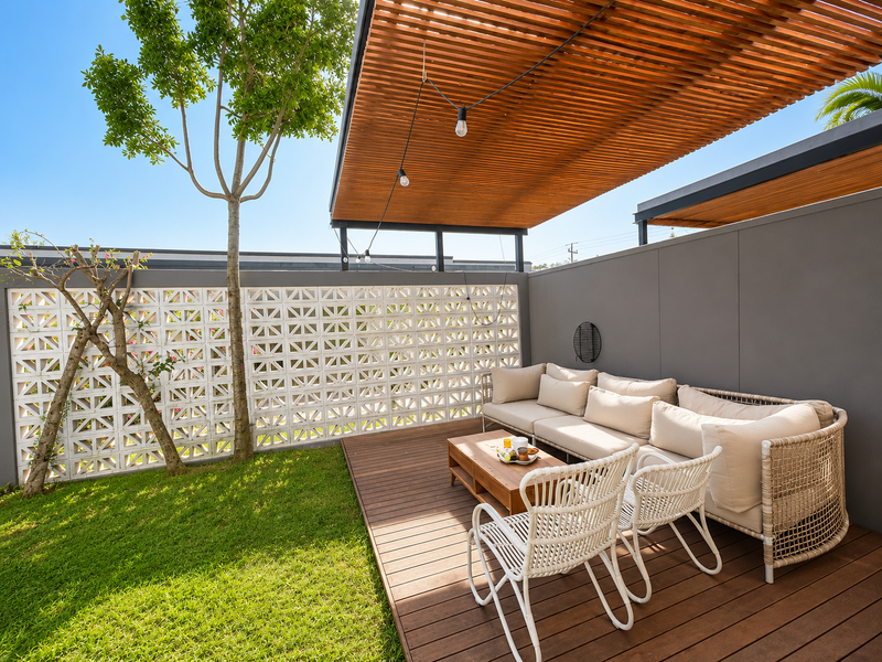 A modern outdoor patio featuring timber decking, a slatted pergola roof, and a decorative breeze block privacy wall overlooking a small garden area.