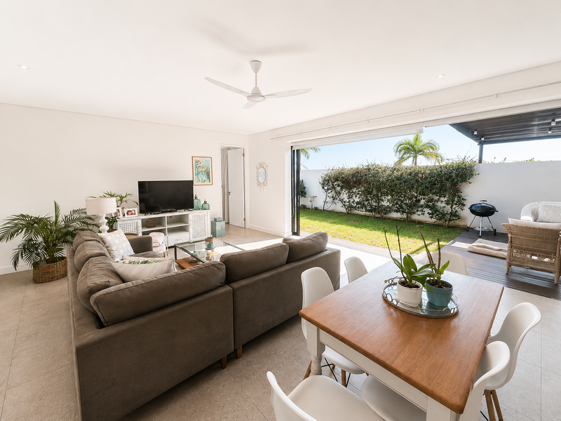 Bright open-plan living and dining area featuring large sliding doors that open onto a private covered patio and garden.
