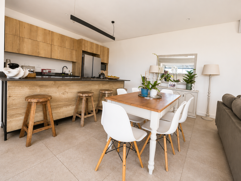 Modern open-plan living area featuring a contemporary kitchen with wood-look cabinetry, dark stone countertops, and seamless tiled flooring throughout the dining and kitchen space.