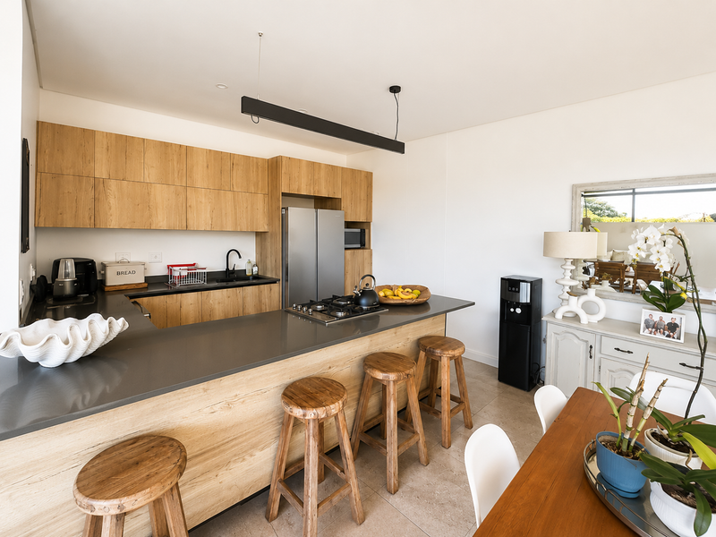 Modern open-plan kitchen featuring light wood cabinetry, stone countertops, gas cooktop, and integrated appliances, seamlessly flowing into the dining area.