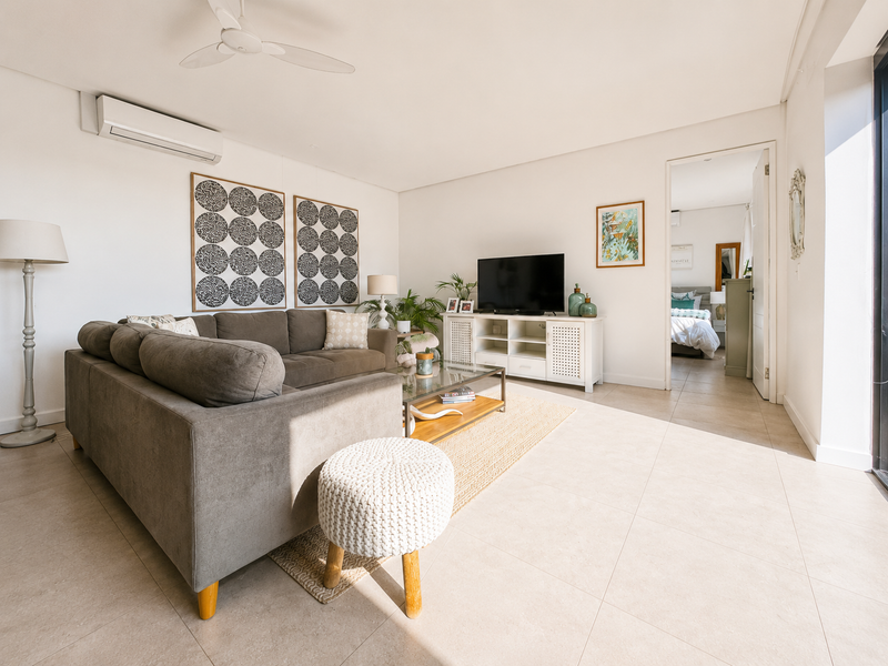 A bright and modern living room featuring tiled flooring, a ceiling fan, and a wall-mounted air conditioning unit with access to an outdoor area.