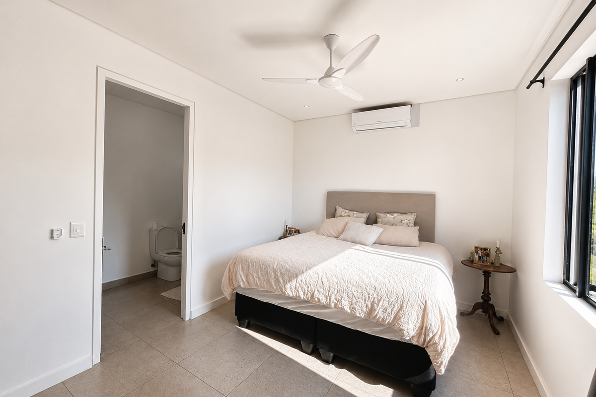 A bright and modern bedroom featuring tiled flooring, a ceiling fan, and a wall-mounted air conditioning unit, with direct access to an en-suite bathroom.