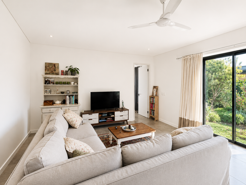 A bright and well-maintained living room featuring tiled flooring, a ceiling fan, and large sliding glass doors providing access to the garden.