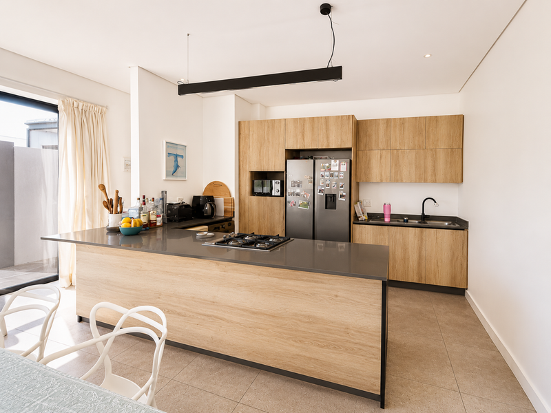 Modern kitchen featuring light wood cabinetry, stone countertops, a central island with a gas cooktop, and integrated appliances.