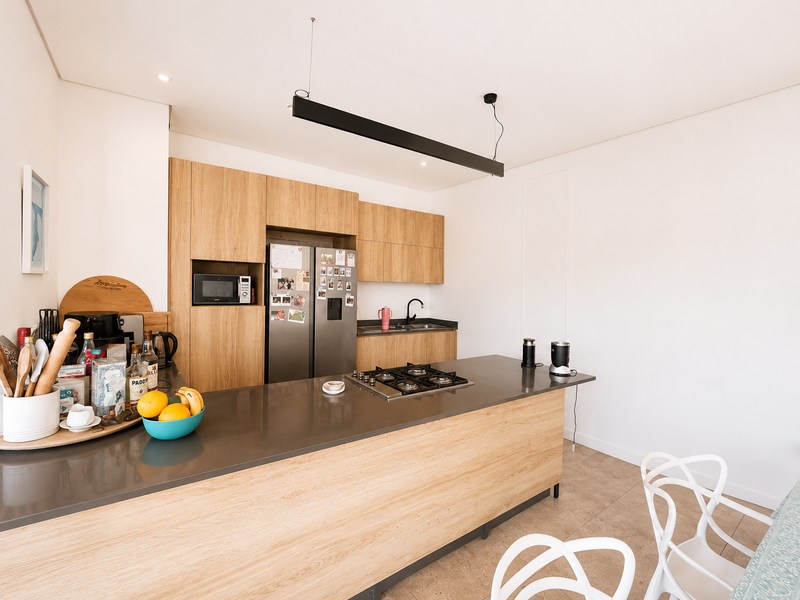 Modern kitchen featuring light wood cabinetry, stone countertops, a central island with a gas hob, and integrated appliances in a clean, contemporary design.