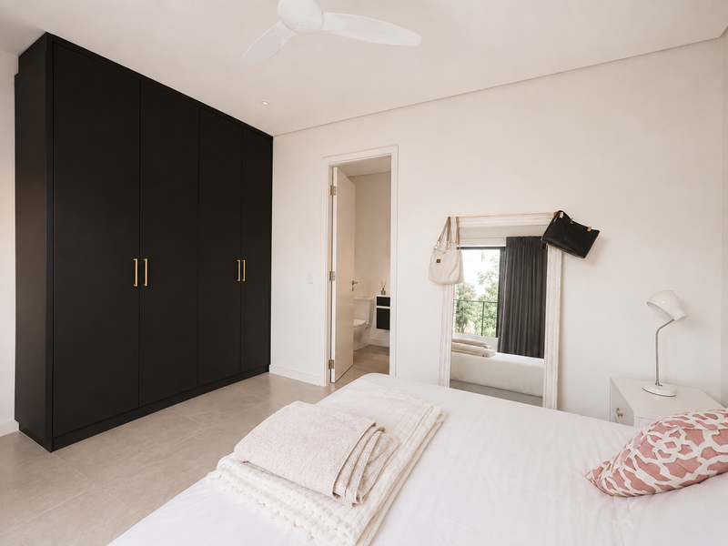 Modern bedroom featuring sleek black built-in wardrobes, neutral tiled flooring, a ceiling fan, and direct access to an en-suite bathroom.