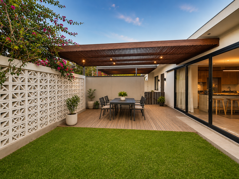 A beautifully landscaped outdoor patio featuring a timber pergola, composite decking, and a decorative breeze block wall, seamlessly connected to the interior living space.