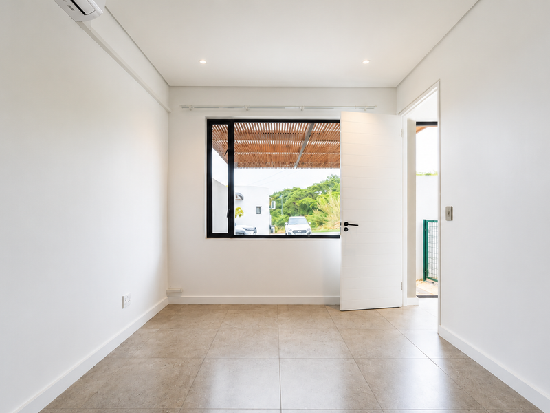 A bright, empty bedroom featuring neutral tiled flooring, recessed lighting, a split-system air conditioner, and a large window with views of the exterior.