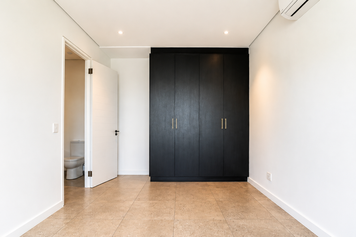 A bright, modern bedroom featuring neutral tiled flooring, a sleek black built-in wardrobe, and an en-suite bathroom.