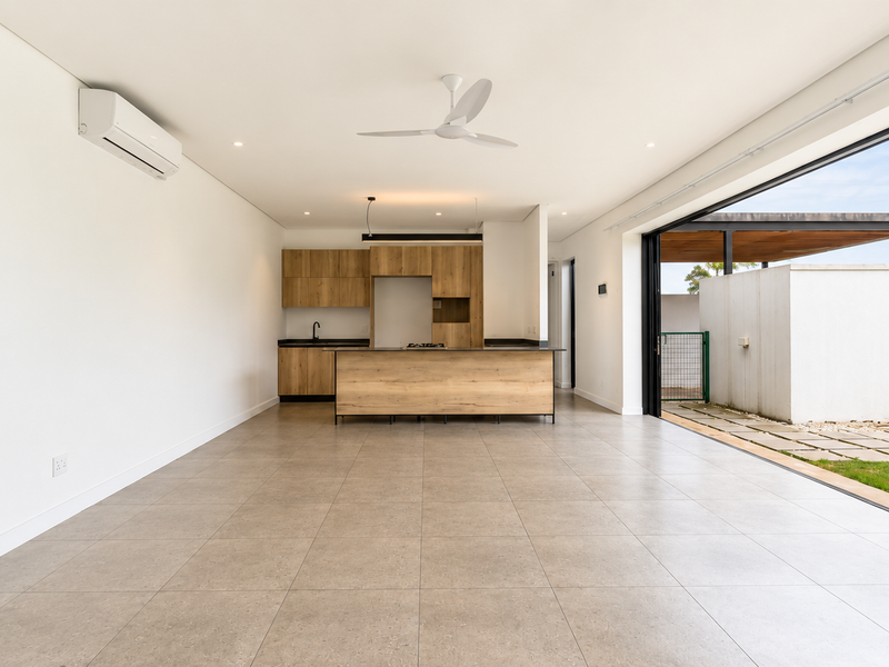 Spacious open-plan living and kitchen area featuring modern wood-finish cabinetry, a central island, and seamless indoor-outdoor flow through large sliding glass doors.