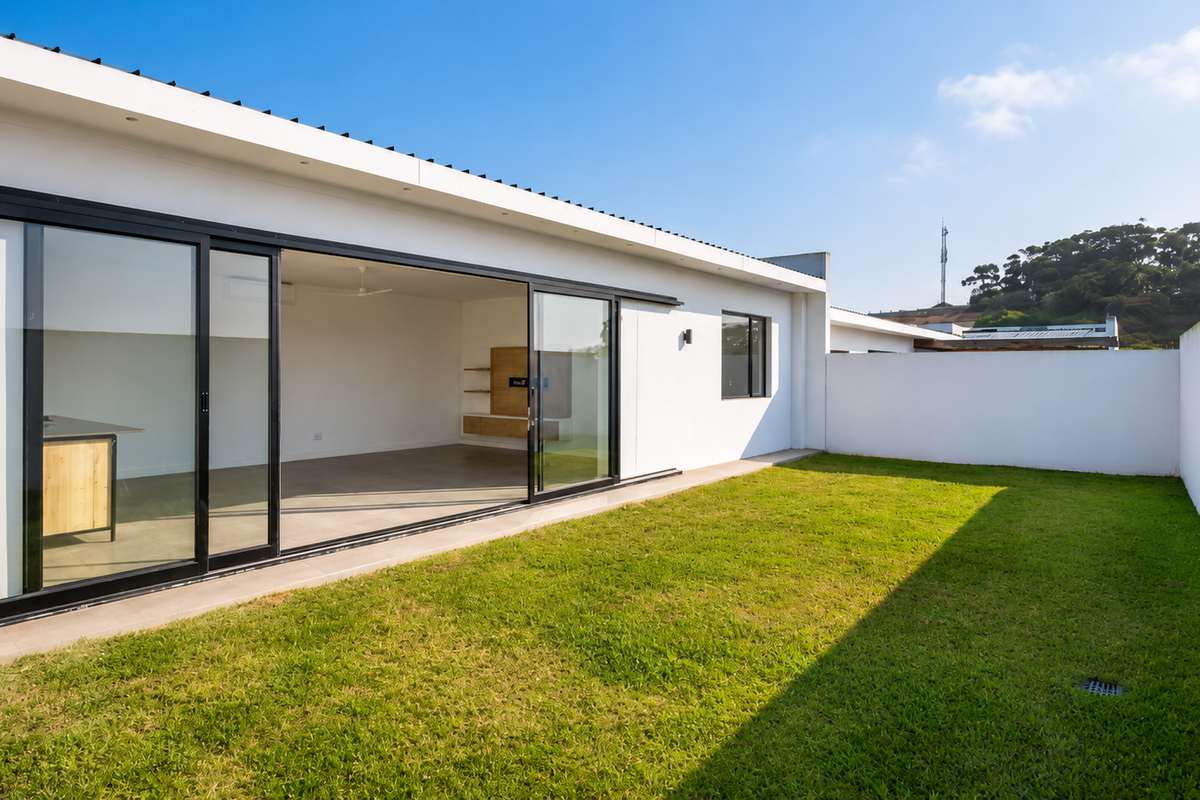 Rear view of the townhouse featuring a well-maintained lawn, boundary wall, and large sliding glass doors opening into the living area.