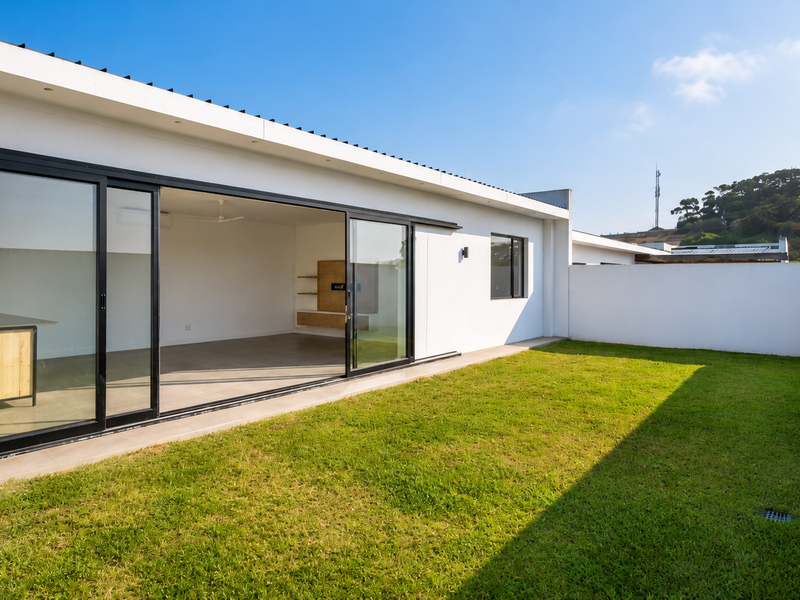 Rear view of the townhouse featuring a well-maintained lawn, boundary wall, and large sliding glass doors opening into the living area.