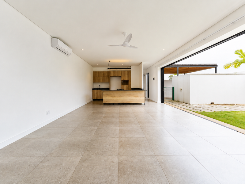 Spacious open-plan living and kitchen area featuring modern wood-finish cabinetry, tiled floors, and seamless indoor-outdoor flow through large sliding doors.