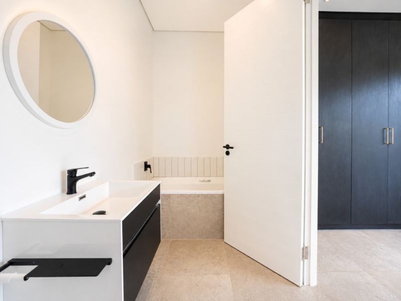 Modern bathroom featuring a sleek vanity with basin, built-in bathtub with tiled surround, and dark cabinetry, finished with neutral floor tiles.