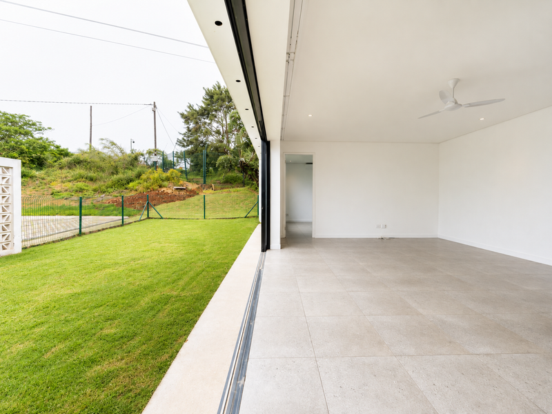 Spacious open-plan living area featuring large format floor tiles, recessed lighting, and seamless indoor-outdoor flow through expansive sliding glass doors to the garden.