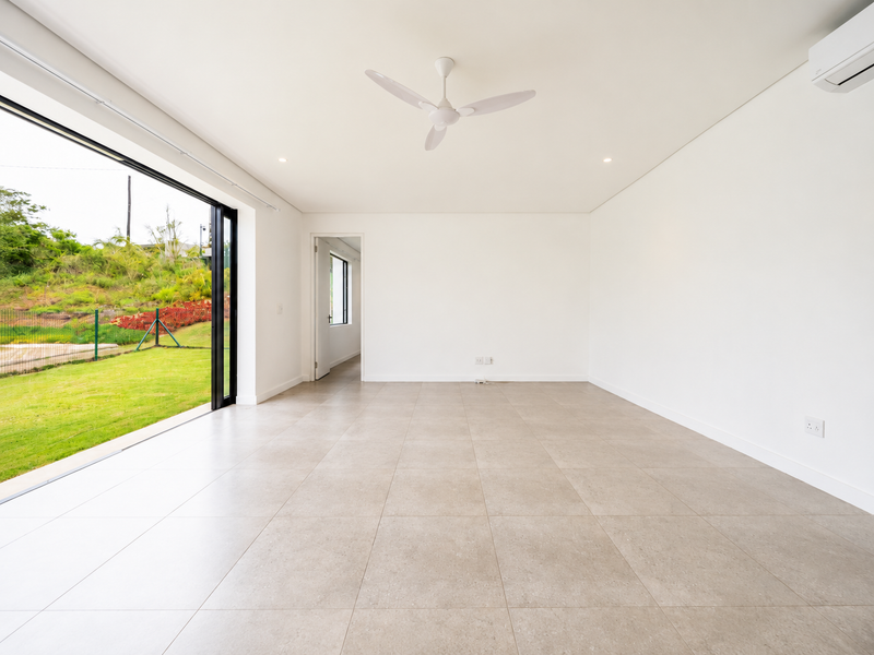Bright and spacious open-plan living area featuring large sliding glass doors, neutral tiled flooring, a ceiling fan, and split-system air conditioning.