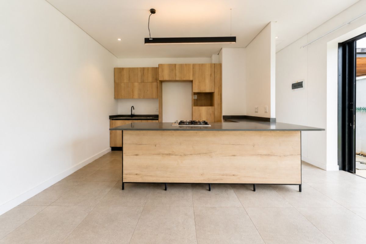 Modern open-plan kitchen featuring light wood cabinetry, a central island with a gas hob, dark countertops, and large format floor tiles.