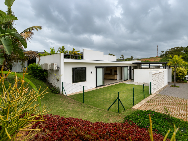 Rear view of a modern townhouse featuring a private garden, paved driveway, sliding glass doors, and a decorative breeze block wall.