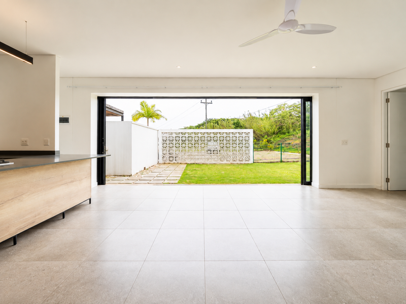 Spacious open-plan living area featuring large format floor tiles, a modern kitchen island, and seamless bi-fold doors opening to a private garden.