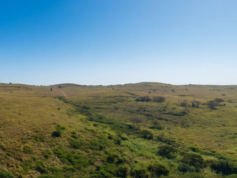An aerial view of expansive, rolling grassland and natural terrain, showcasing the open landscape of the vacant residential property.