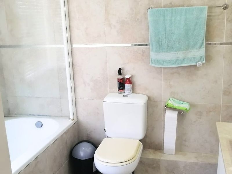 A functional bathroom featuring tiled walls, a bathtub with a glass shower screen, and a standard toilet.